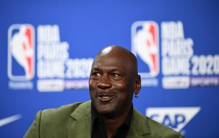 Michael Jordan sedí v zeleném saku, za ním je modré pozadí